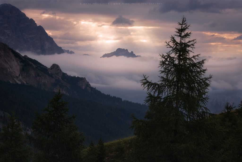 One of the peaks of the Dolomites emerges from morning low cloud as the first rays of light penetrate the cloud