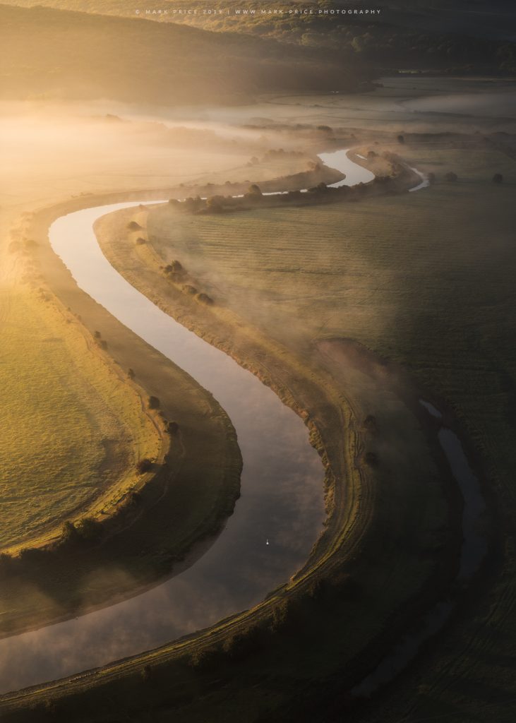 The meandering Cuckmere river in East Sussex at first light as a single swan glides along the water