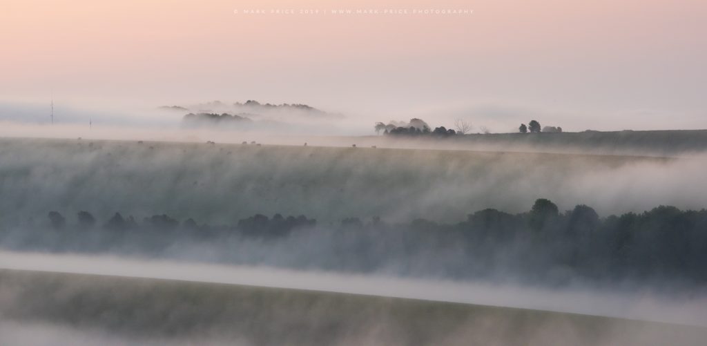 A wave of morning mist passes over a ridge line on the South Downs, Sussex