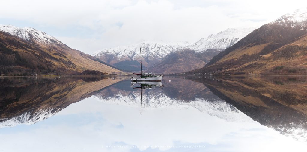 A perfectly placed boat is mored behind the dramatic hills of the Scottish Highlands