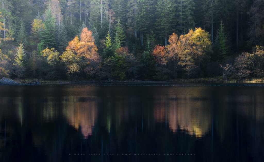 Beautiful shades of Autumn reflect in a still loch, The Trossachs, Scotland